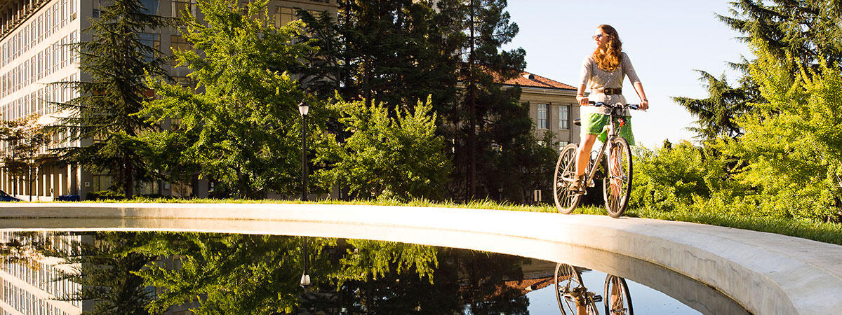 woman on a bicycle near a reflecting pool outside Hearst Mining building