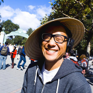 student with straw hat smiling in the sun in Sproul Plaza